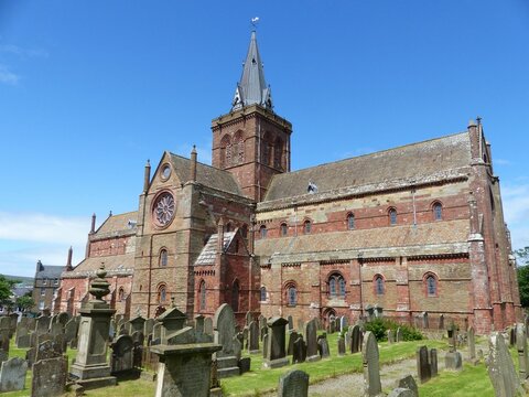 St Magnus Cathedral with graves on a cemetery in Kirkwall, Scotland with blue sky