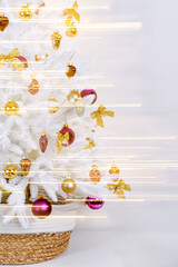 White Christmas tree in a wicker basket decorated shiny and gold decorations, bows, balls, toys and with luminous garland on light background. Merry Christmas and Happy Holidays!