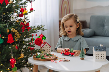 Christmas holidays. A little girl plays with toy cars, little houses and christmas decorations. Holiday Activity for Kids. Merry Christmas and Happy Holidays!