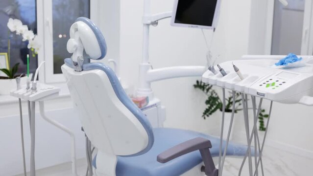 overall shot of empty modern white and light blue dentist office in clinic with equipment, computer, professional dental chair and drilling machine.
