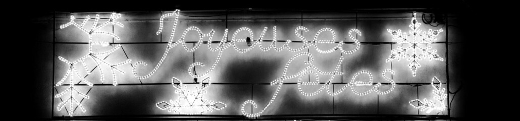 Joyeuses fêtes winter holidays glowing decoration at city billboard. France. Happy holidays greeting in French. Black white istoric photo