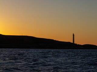 Breathtaking view of orange sunset sky and lighthouse silhouette above the sea - beautiful wallpaper