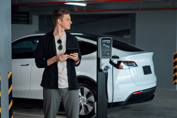 Young man travel with EV electric car to shopping center parking lot charging in downtown city...