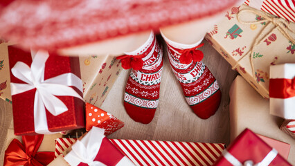 Fototapeta premium A woman, cozy and warm in a cute red socks, poses by Christmas tree, box gifts