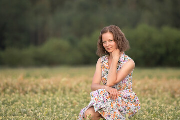Naklejka na ściany i meble Portrait of a young beautiful girl in a light dress on a summer field.