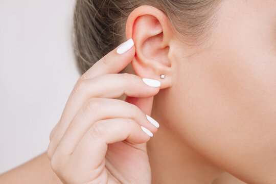 Ear piercing. Cropped shot of a young woman wearing elegant stud earrings on a gray background. Jewelry with gemstones, accessories
