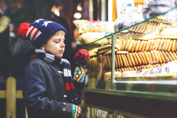 Happy child eating on apple covered with red sugar on Christmas market