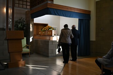 Two mourners standing in front of a coffin on a Bier at a crematorium. 