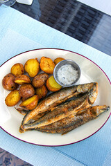 Fried smelt with boiled potatoes and mushroom sauce on a white plate. Delicious rustic lunch