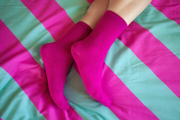 Pink obsession concept. Male legs on bed. Pink socks on feet. Close up. Text space. Indoor shot