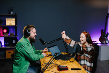 A podcast host and a guest have fun chatting during a live online broadcast in a home studio.