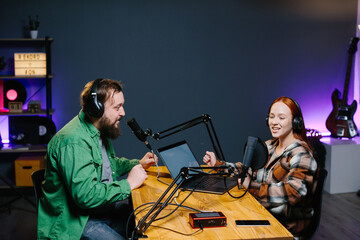 A podcast host and a guest have fun chatting during a live online broadcast in a home studio.