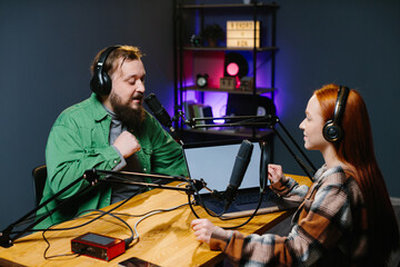 A podcast host and a guest have fun chatting during a live online broadcast in a home studio.
