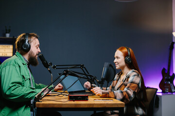 A podcast host and a guest have fun chatting during a live online broadcast in a home studio.