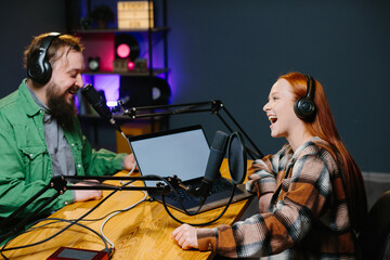 A podcast host and a guest have fun chatting during a live online broadcast in a home studio.