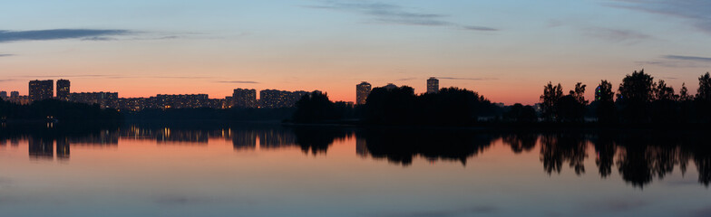 Panorama of the evening city on the river bank, sunset.