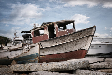 An old broken wooden fishing boat against the background of modern yachts.