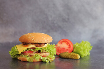Double cheeseburger and vegetables on a gray background. Juicy tasty burger close-up, side view. Fast food