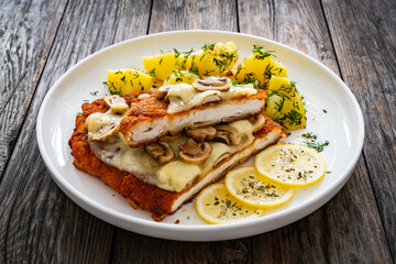 Crispy breaded seared chicken cutlet with fried white mushrooms, cheese and boiled potatoes on...