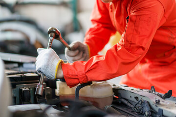 Automobile technician working in auto garage, technician holding a wrench preparing to repair broken vehicle. Professional auto or car repairman fixing a crashed car.