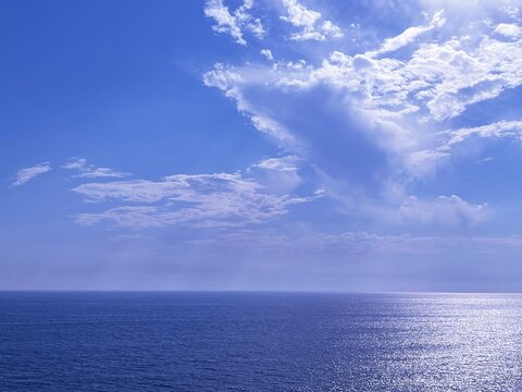 Sky clouds over shiny blue sea water.