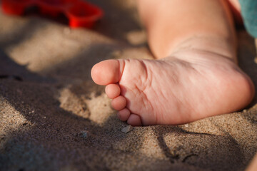 Cute foot with the fingers of a small child on the sand on the beach