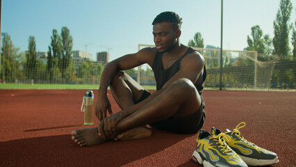Sad unwell African American man sportsman runner athlete footballer suffering painful damaged foot...