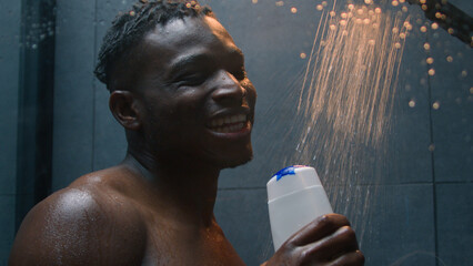 Happy funny African American man guy singing in bathroom ethnic joyful bare male sing song in...