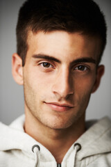 Obraz premium Portrait, confident and man in hoodie for fashion isolated on gray studio background. Serious young person, face of model and clothes, casual style and cool student in trendy streetwear in Spain