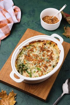 Green bean casserole with creamy sauce topped with crispy fried onions in a white ceramic dish on a green concrete background. Traditional Thanksgiving Dishes. American cuisine.