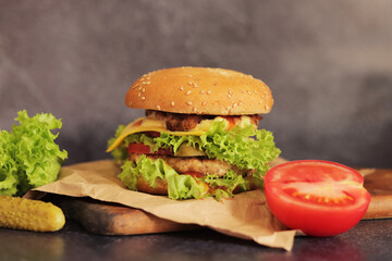 Double cheeseburger and vegetables on a gray background. Juicy tasty burger close-up on a wooden cutting board, side view. Fast food
