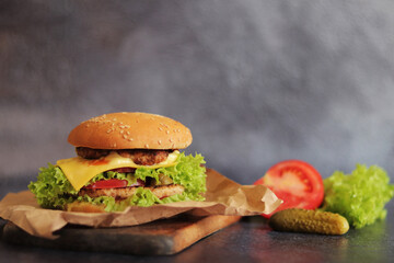 Double cheeseburger and vegetables on a gray background. Juicy tasty burger close-up on a wooden cutting board, side view. Fast food