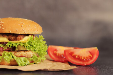 Double cheeseburger and vegetables on a gray background. Juicy tasty burger close-up, side view. Fast food