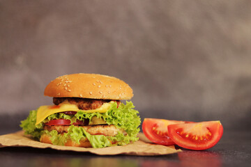 Double cheeseburger and vegetables on a gray background. Juicy tasty burger close-up, side view. Fast food