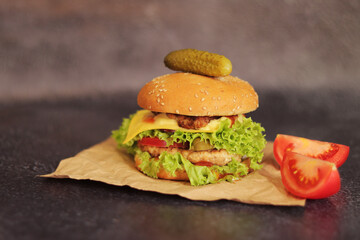 Double cheeseburger and vegetables on a gray background. Juicy tasty burger close-up, side view. Fast food