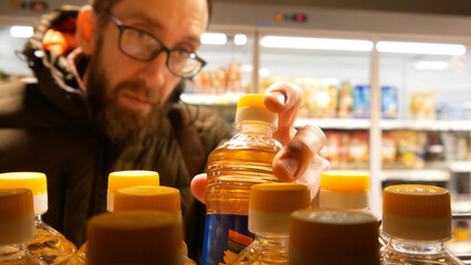 Close-up of many sunflower oil bottles on a supermarket shelf and a male buyer chooses one