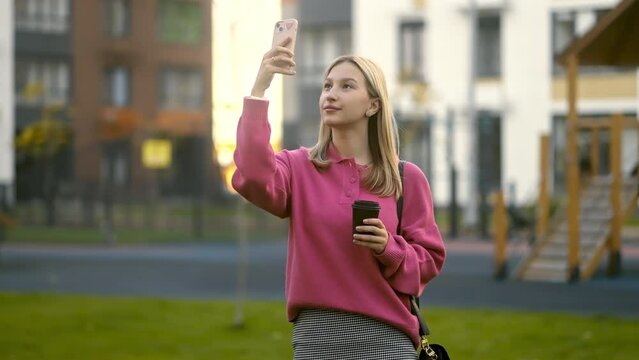 A girl blogger with a phone in her hands is conducting a live broadcast, on the territory of a modern residential complex with well-thought-out architecture for modern life
