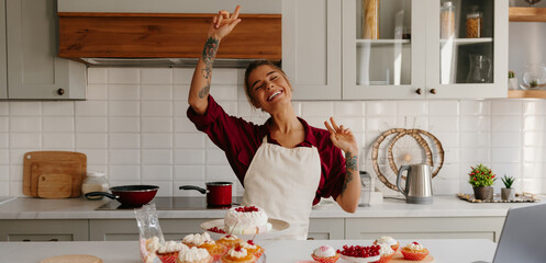 Joyful female baker in apron dancing while making cakes and muffins at the domestic kitchen