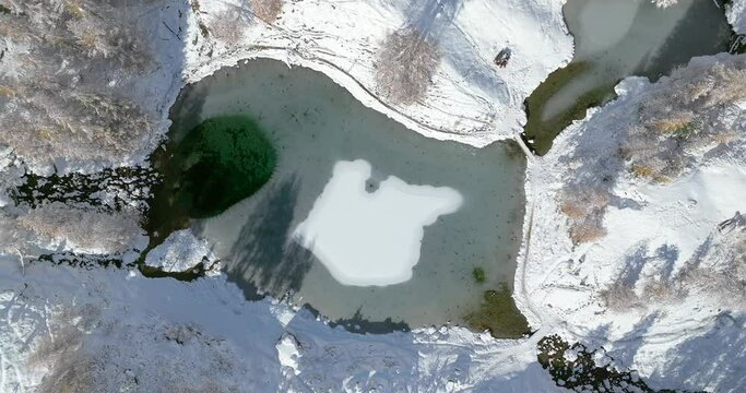 Lac Bleu Arolla lake frost in autumn colors in winter time snow covered Swiss mountains in Switzerland orange colors daylight flowing stream river aerial by drone