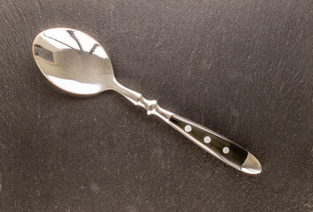 One metal spoon on slate stone, macro, top view.