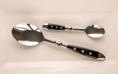 Two metal spoons on a ceramic dish, macro, top view.