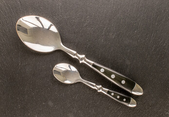 Two metal spoons on slate stone, macro, top view.