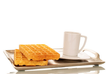 Two freshly baked aromatic waffles with ceramic saucer and cup on metal tray, macro, isolated on white background.