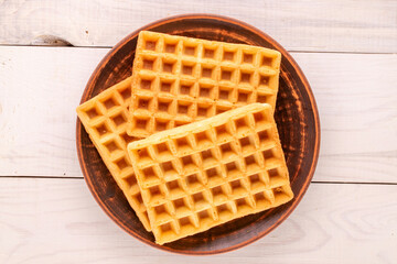 Three freshly baked aromatic waffles on a clay plate on a wooden table, macro, top view.