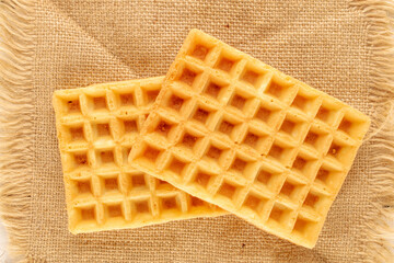 Two freshly baked aromatic waffles on a jute cloth, macro, top view.