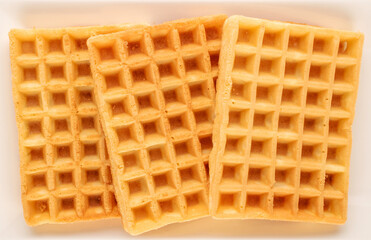 Three freshly baked aromatic waffles on a ceramic white plate, macro, top view.