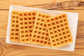 Four freshly baked aromatic waffles on a ceramic white plate on a wooden table
