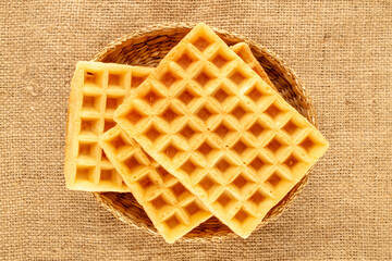 Three freshly baked aromatic waffles with a straw plate on a jute cloth, macro, top view.