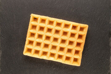 One freshly baked aromatic waffle on slate stone, macro, top view.