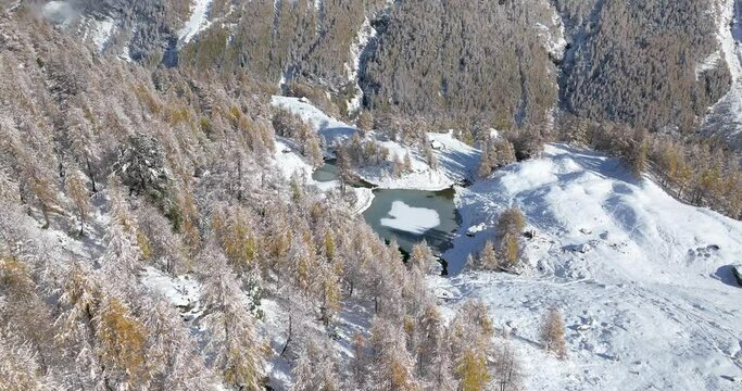 Lac Bleu Arolla lake frost in autumn colors in winter time snow covered Swiss mountains in Switzerland orange colors daylight flowing stream river aerial by drone